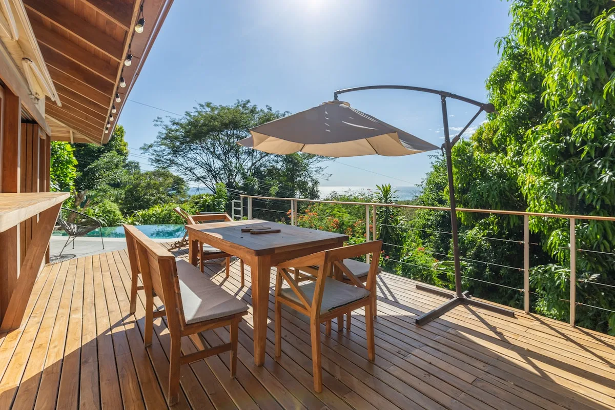 Comedor al aire libre en una terraza de madera, con una mesa bajo una sombrilla.