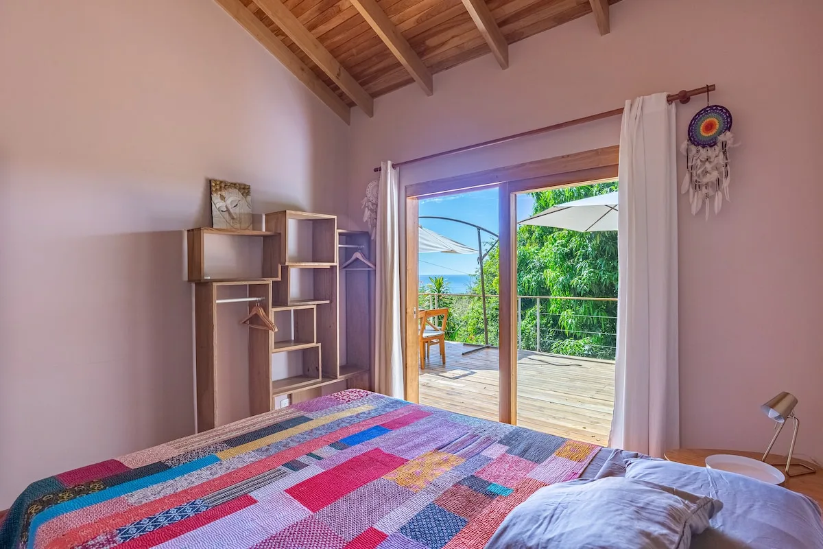Un dormitorio con una colcha colorida de retazos y puertas abiertas a una terraza de madera.