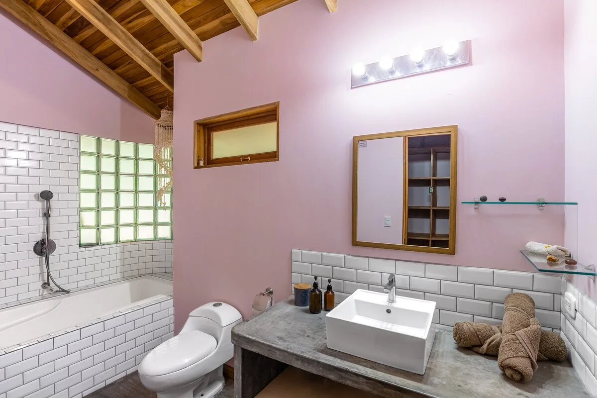 Un baño alicatado con lavabo, inodoro y ducha bajo un techo de madera.