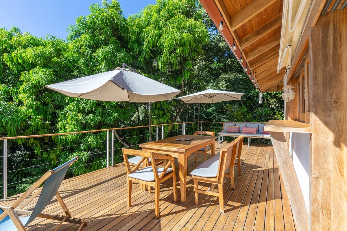 Una terraza de madera tiene una mesa de comedor, asientos y dos sombrillas.