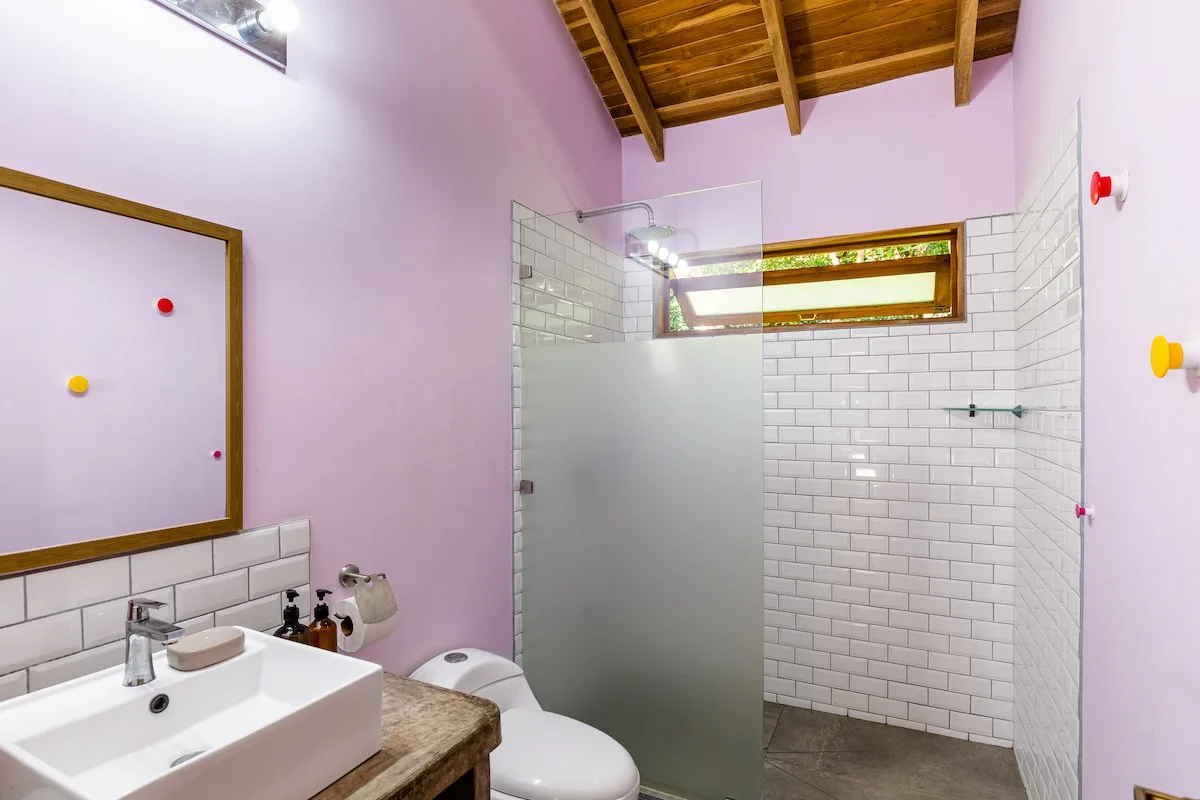 Un baño con lavabo, inodoro y zona de ducha con azulejos bajo un techo de madera.
