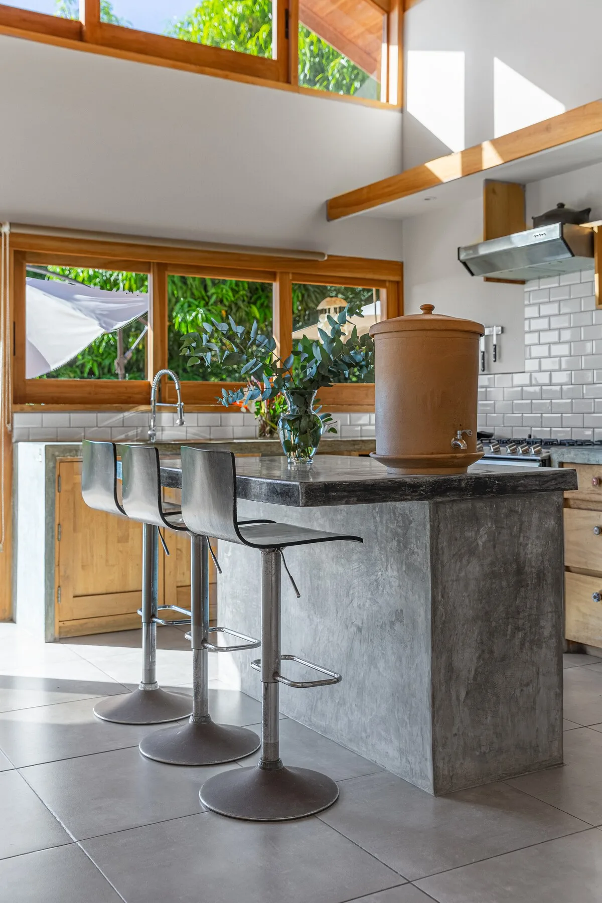 Una cocina luminosa con una isla de piedra y asientos de metal.