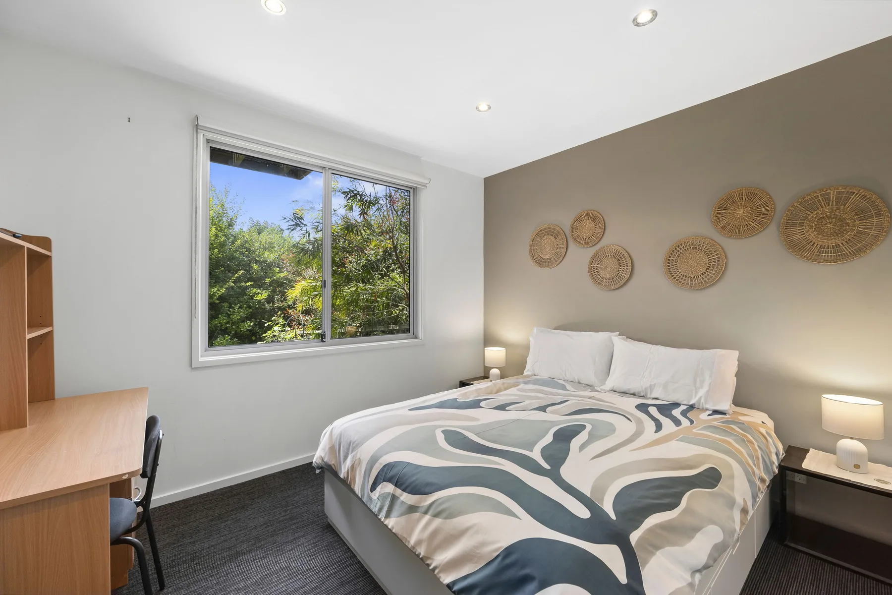 A bright bedroom with a bed, patterned bedding, and a large window.