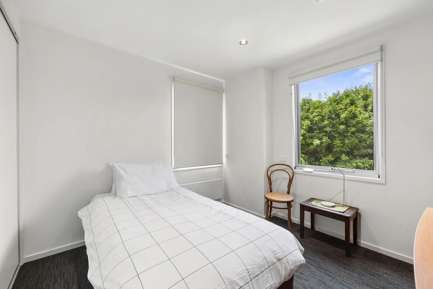 A bright bedroom with a bed, a chair, and a large window overlooking greenery.