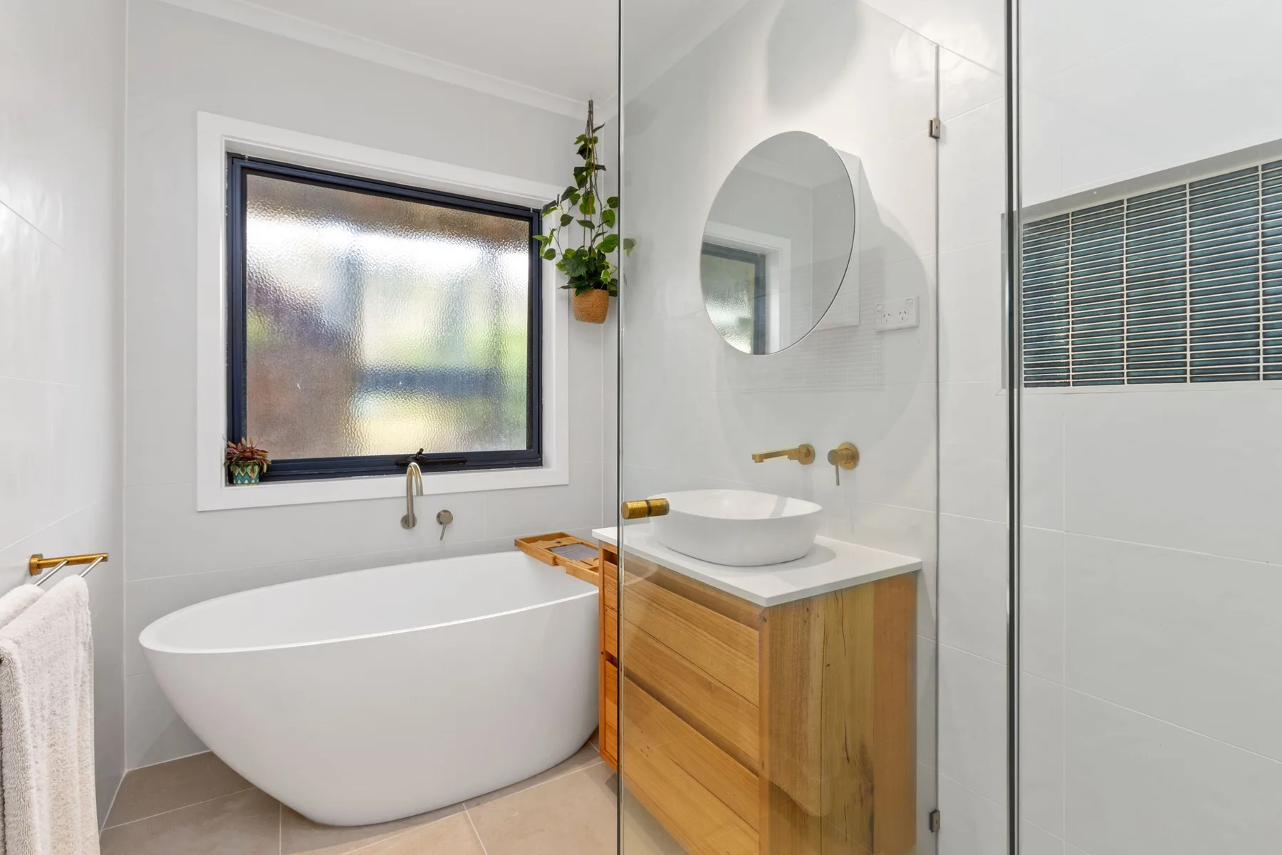 Un baño luminoso cuenta con una bañera, un mueble de lavabo y un espejo redondo.