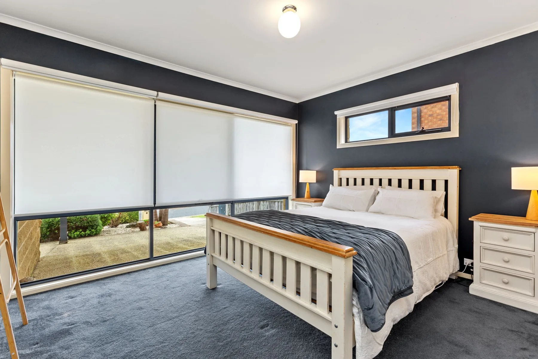 Un dormitorio con una cama, paredes oscuras y amplias ventanas con persianas.