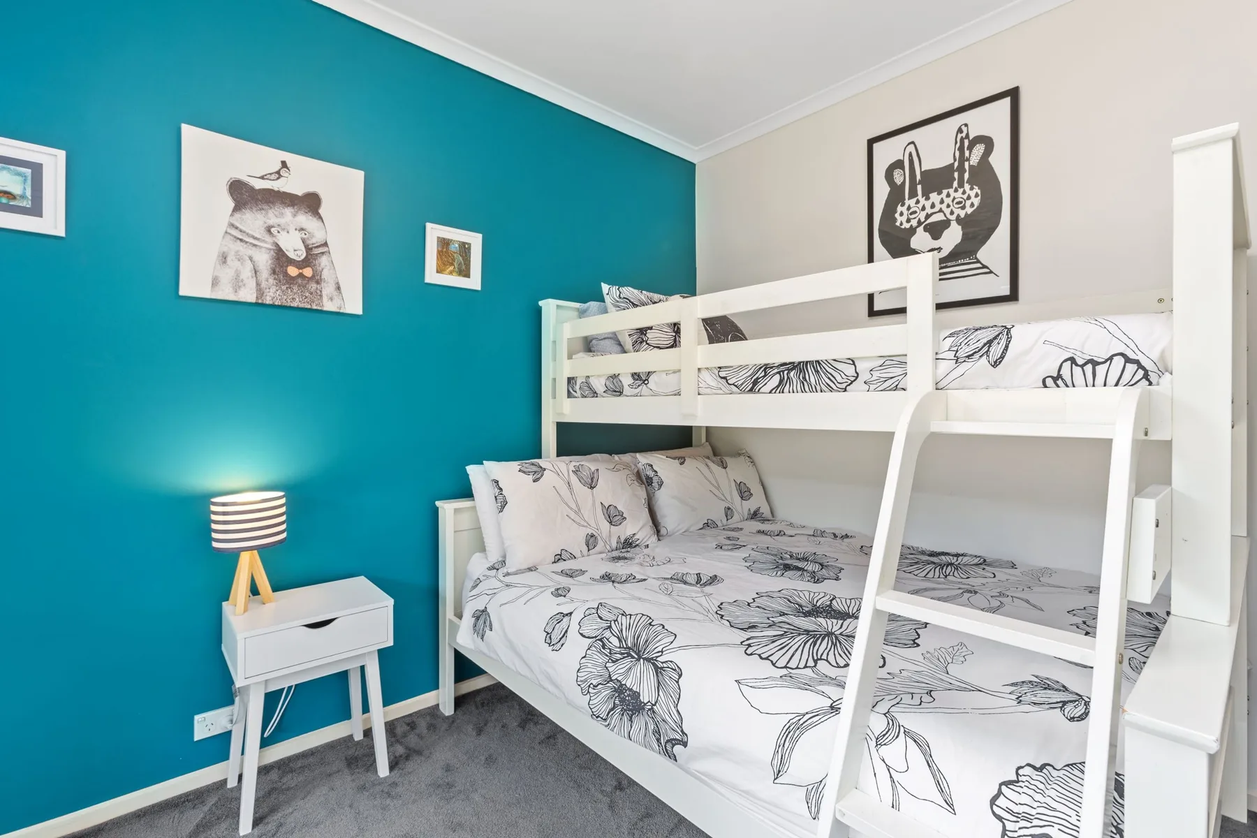 Un dormitorio con una litera blanca y ropa de cama floral junto a una pared verde azulado.