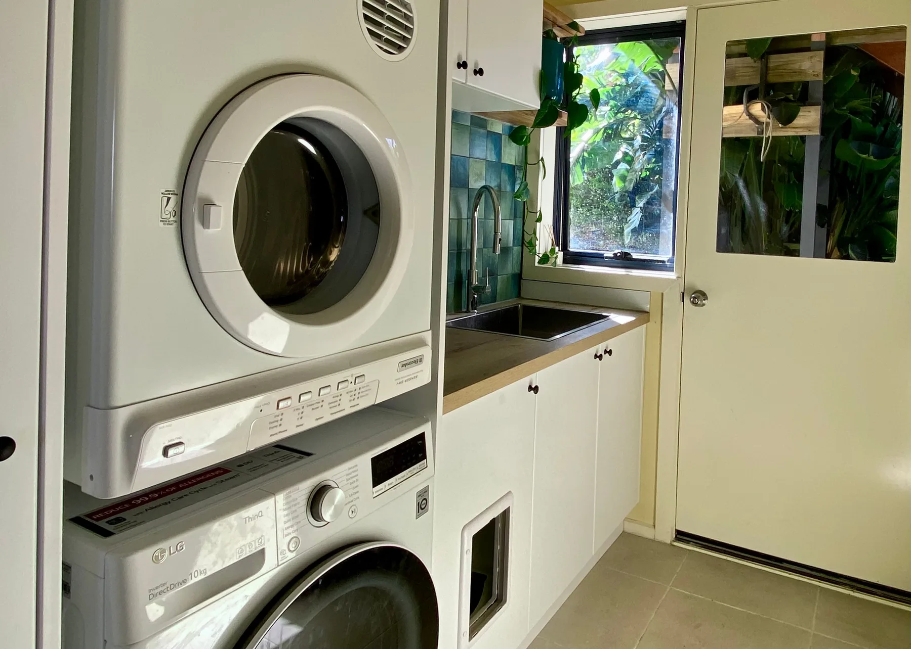 Un cuarto de lavado compacto con lavadoras apiladas junto a una encimera y una ventana.
