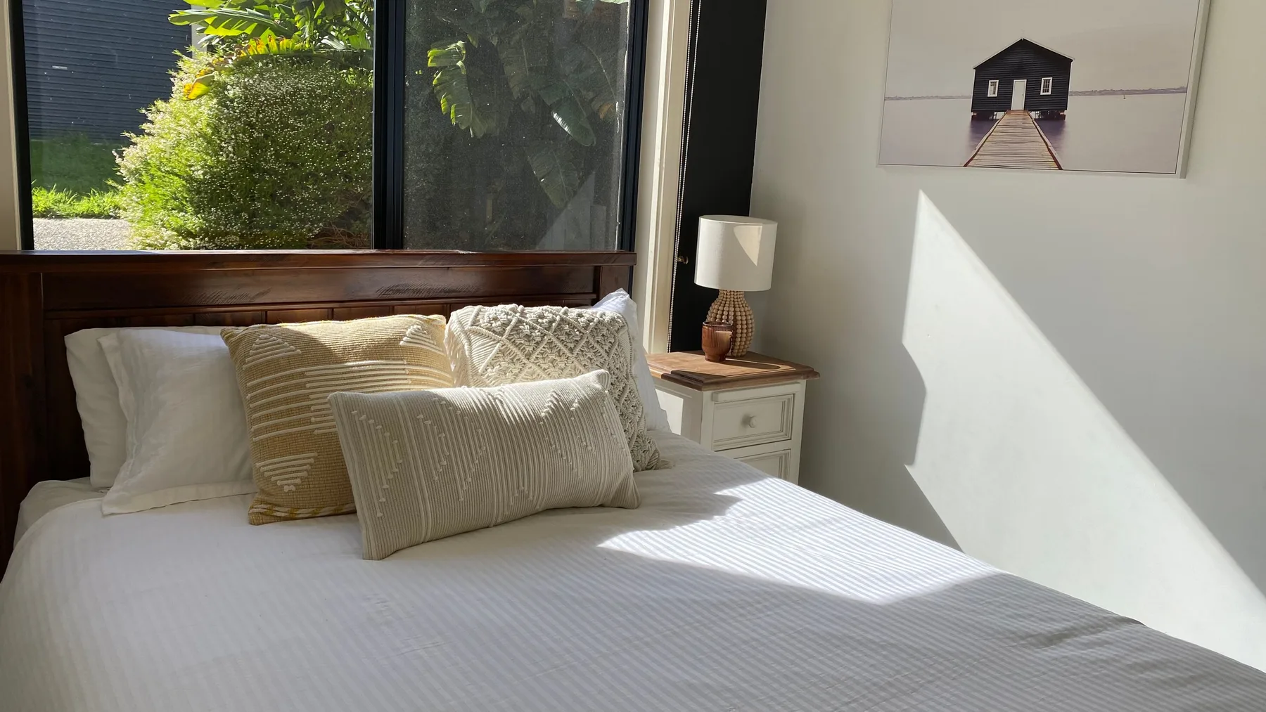 Un dormitorio con una cama bien tendida bajo una ventana grande.