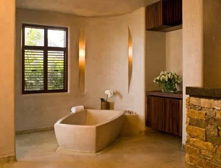 A warm-toned bathroom features a freestanding bathtub, a shuttered window, and a dark wood vanity.