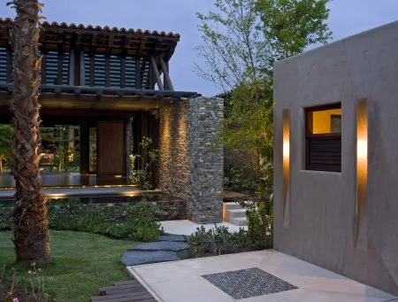 A modern courtyard features a stone path, landscaped garden, and a warmly lit window in a concrete wall.