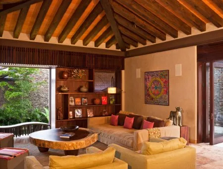 Living room with exposed wooden ceiling beams, a sofa, armchairs, and a round wooden coffee table.