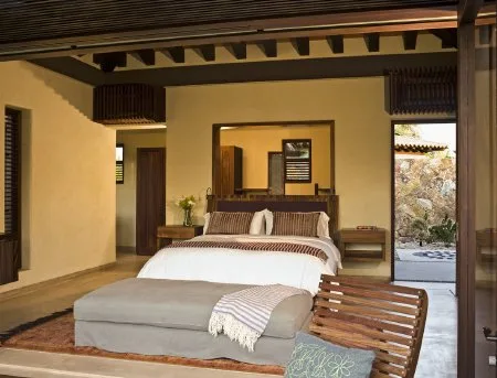 A bedroom with a large bed, upholstered bench, and open doorway leading to a patio.