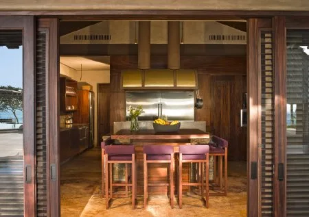 A wooden kitchen and dining area features a long counter, several bar stools, and warm wood cabinetry.