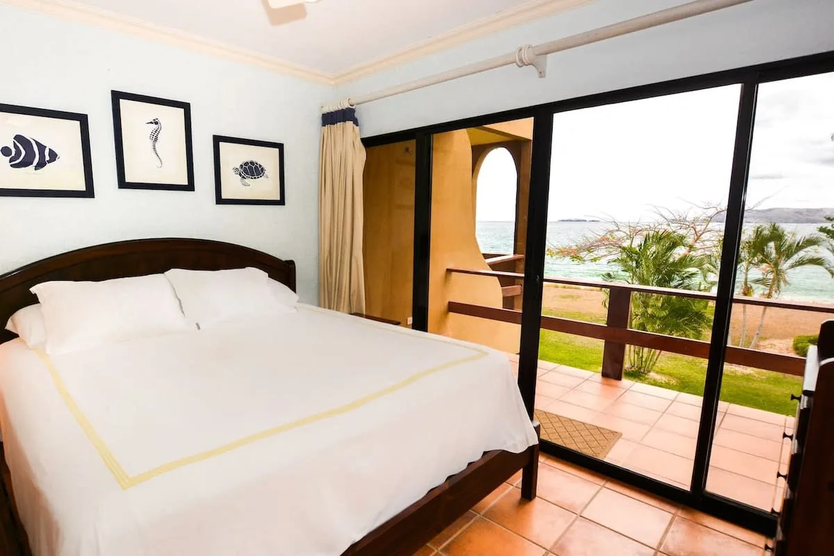 A bedroom with a neatly made bed beside glass doors opening onto a balcony.