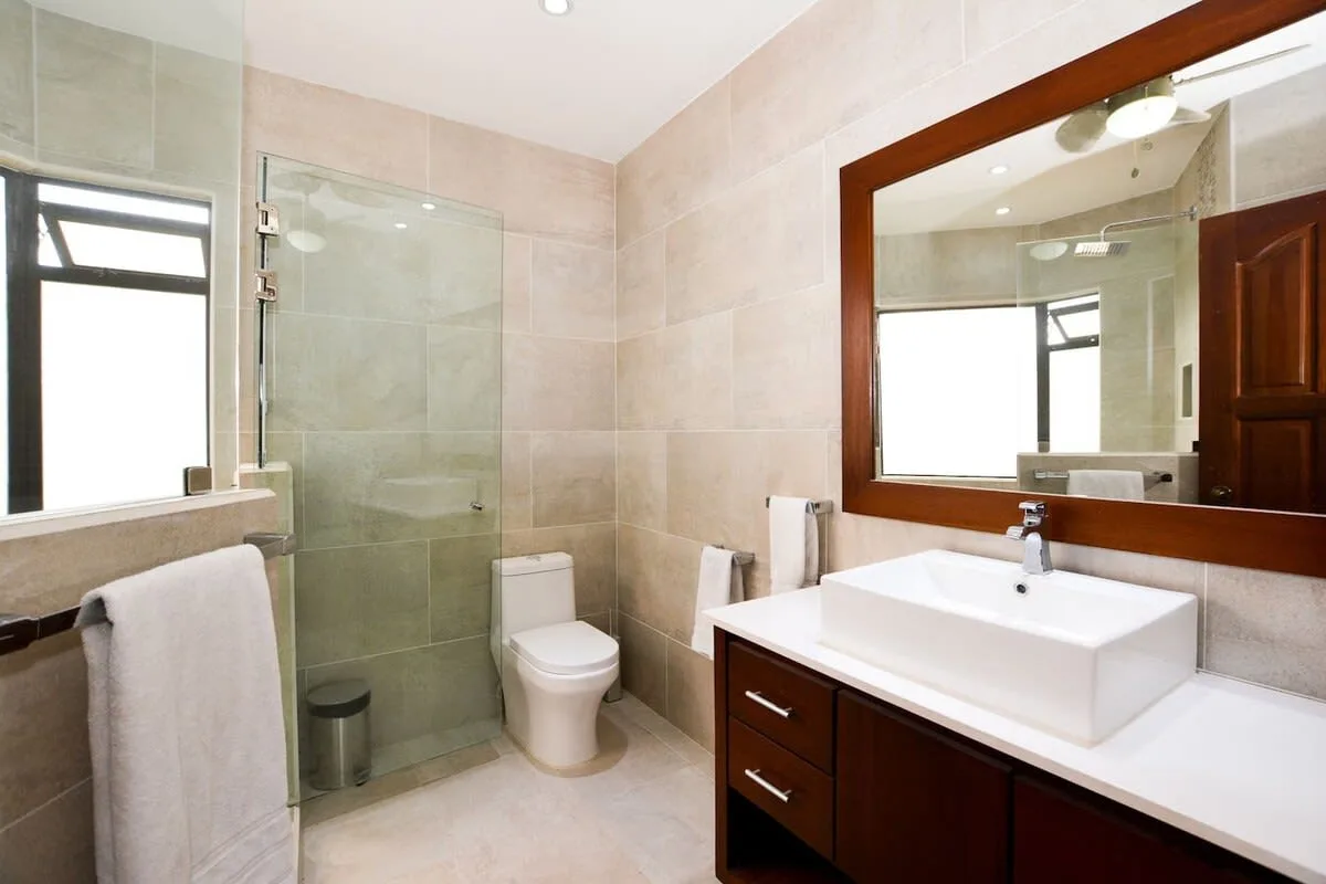 A tiled bathroom with a glass shower, toilet, and sink vanity.