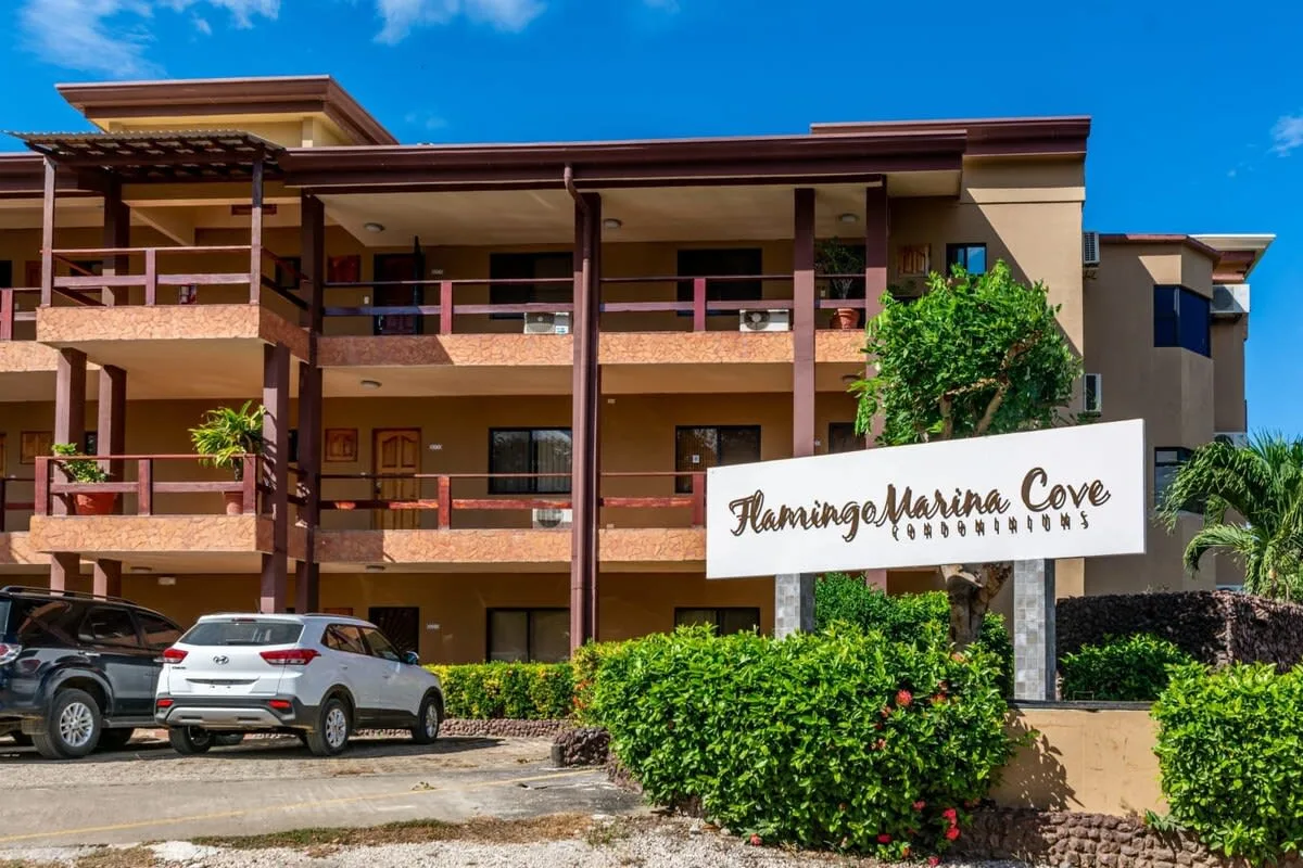 Shared amenity: A multi-story building with balconies stands behind a landscaped sign and parked cars.