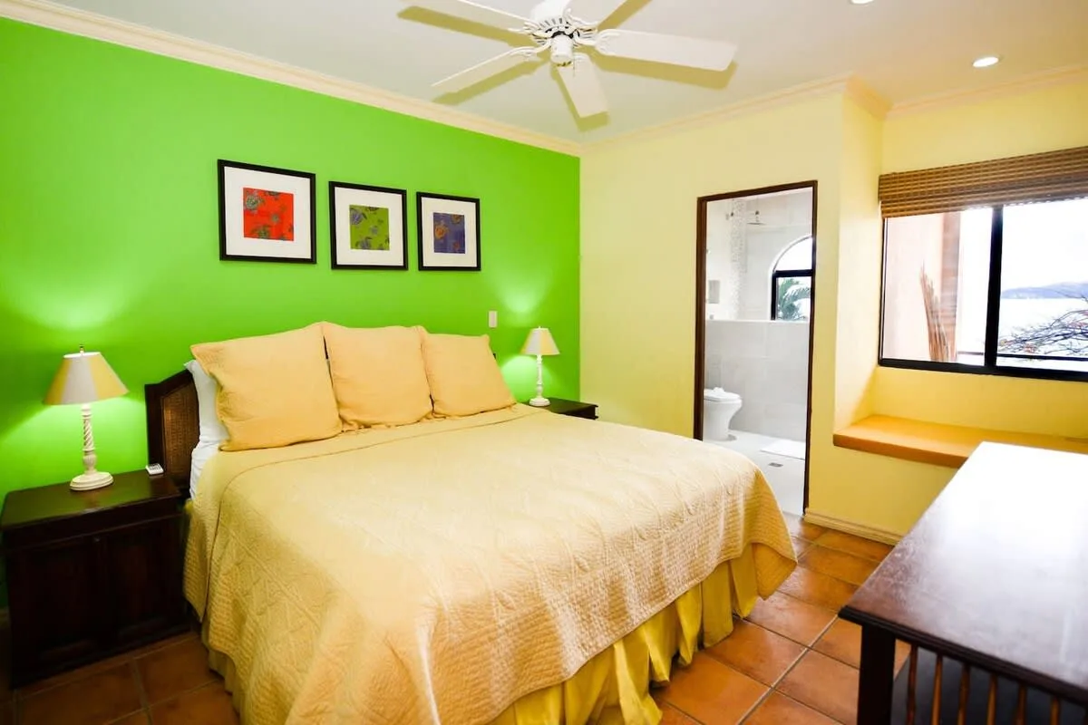 A bedroom with a large bed, green accent wall, and window.