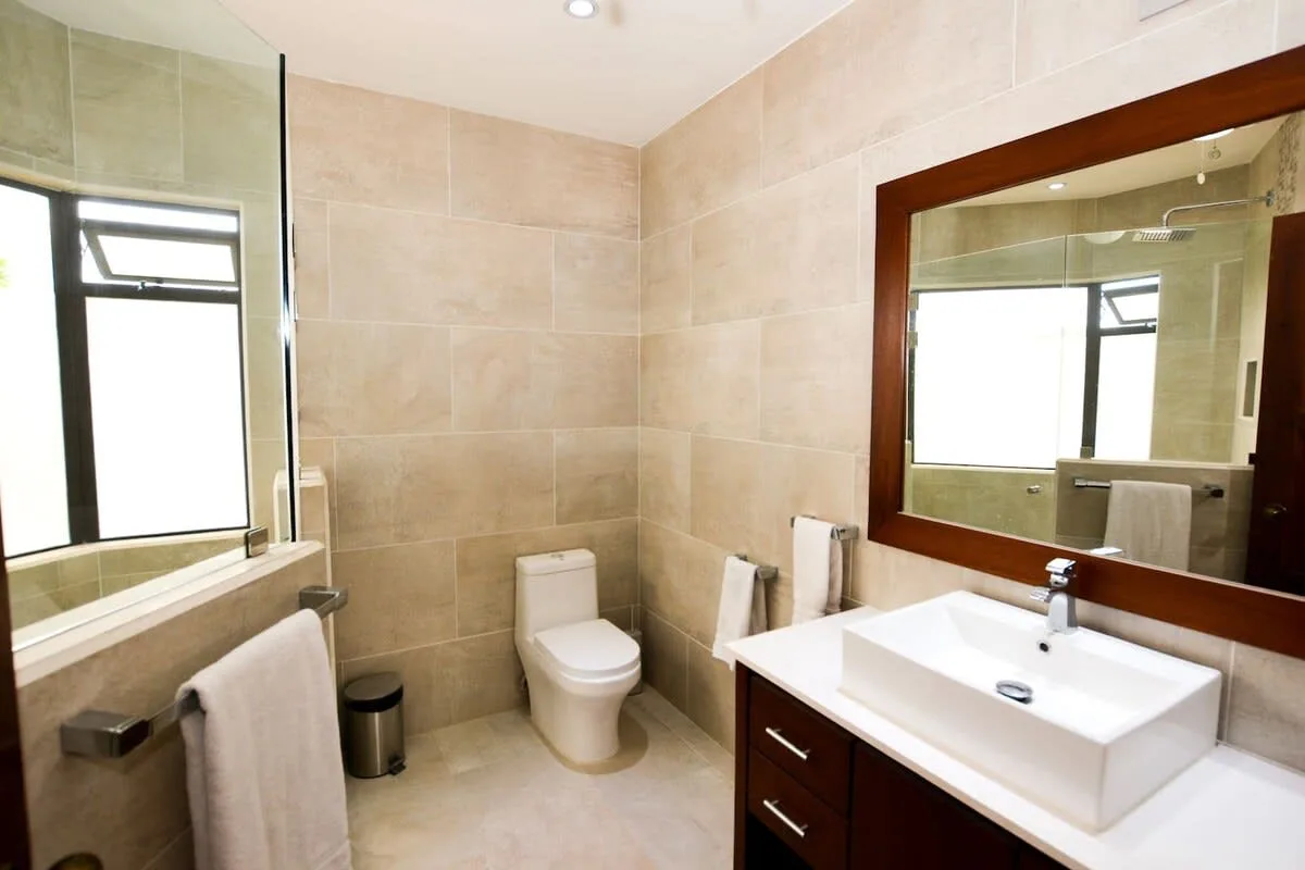 A tiled bathroom with a toilet, sink, and large wall mirror.
