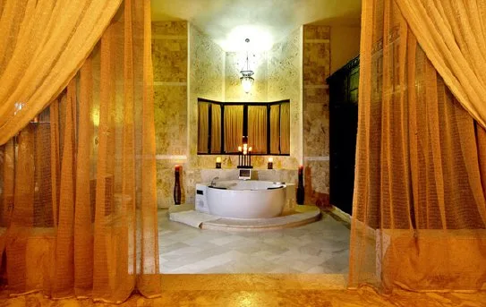 A bathroom with a round tub, framed by golden curtains.
