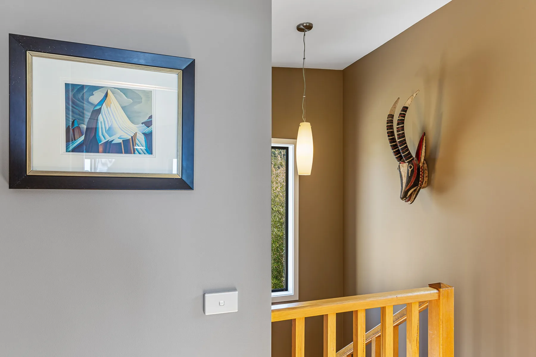 A stair landing with a wooden railing, wall art, and a hanging light.