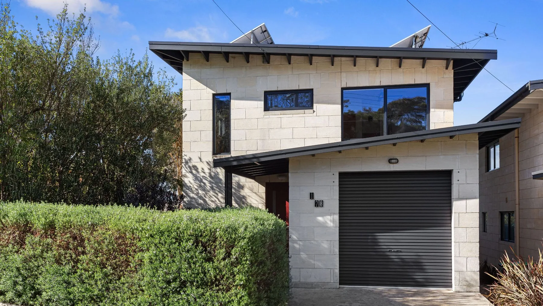 A modern two-story house with a dark garage door and hedges in front.