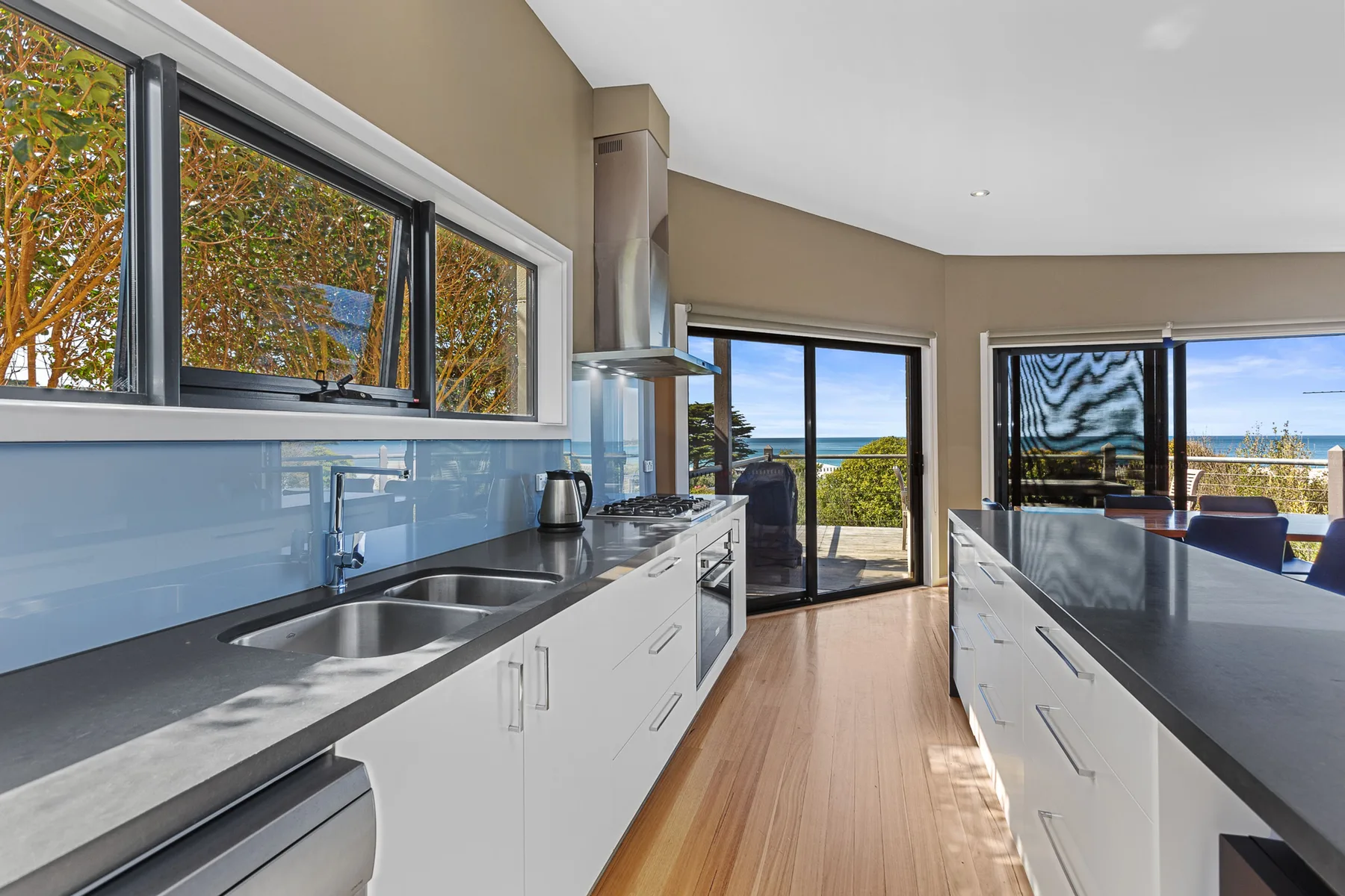 A modern kitchen with long counters and glass doors opening to an outdoor view.