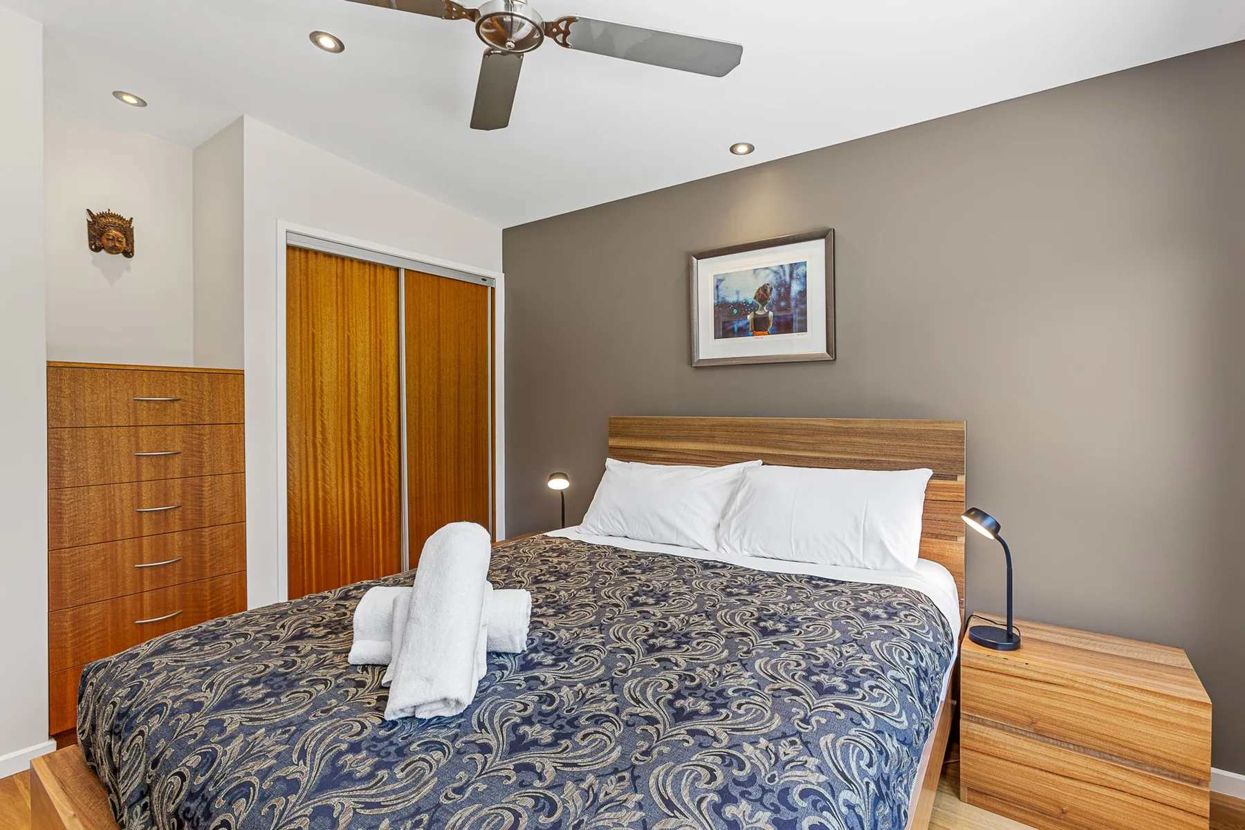 A bedroom with a bed, patterned bedding, and wooden furnishings.