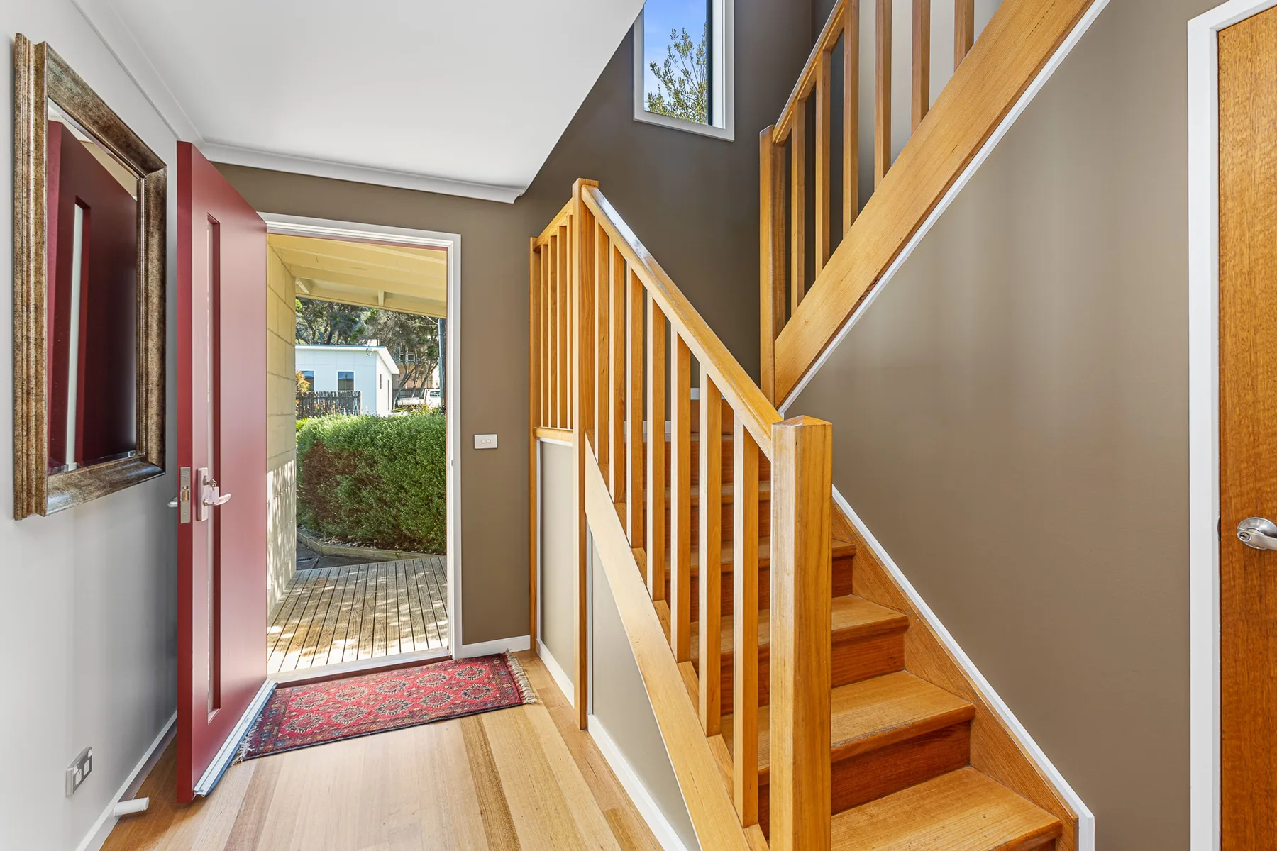 An entryway opens beside a wooden staircase, with an open door to the outside.