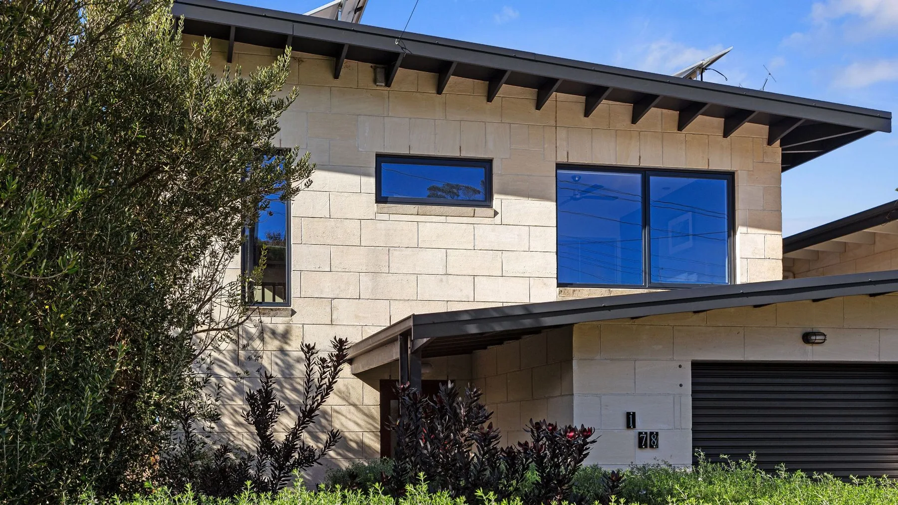 A modern two-story house with pale stone walls and large blue windows.
