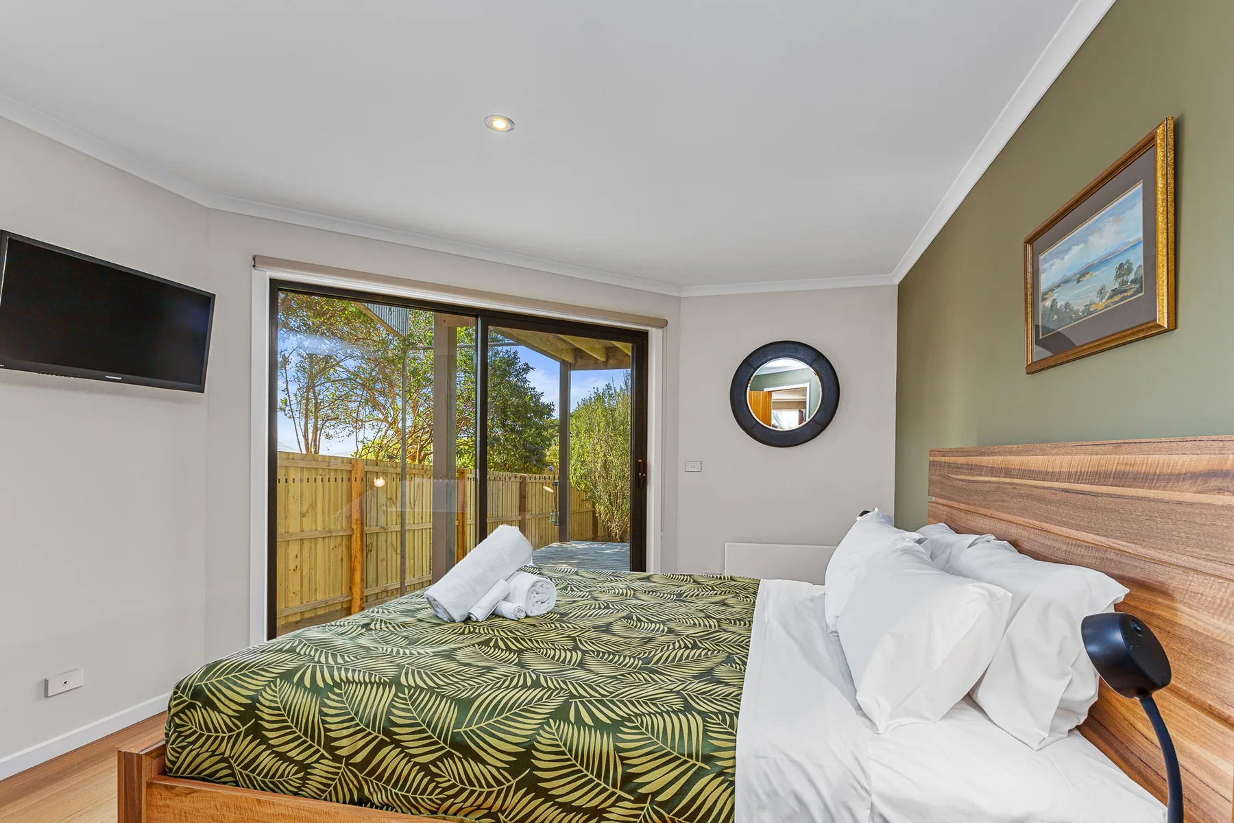 A bedroom with a patterned bedspread and sliding glass doors opening to a fenced yard.