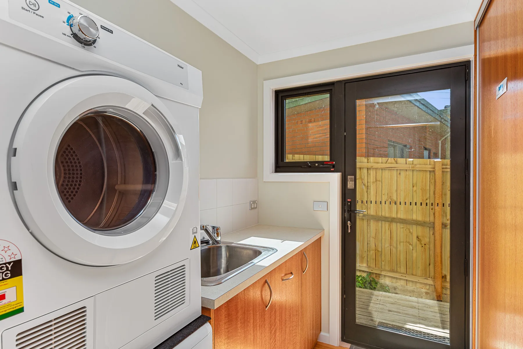 A laundry area with a front-loading washing machine, sink, and glass door.