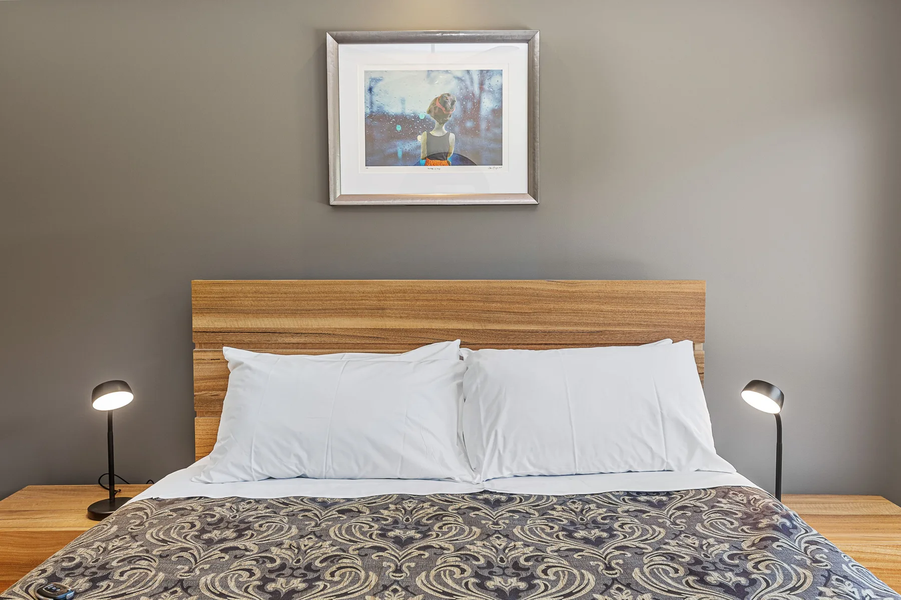 A bedroom with a neatly made bed, patterned bedding, and matching bedside lamps.