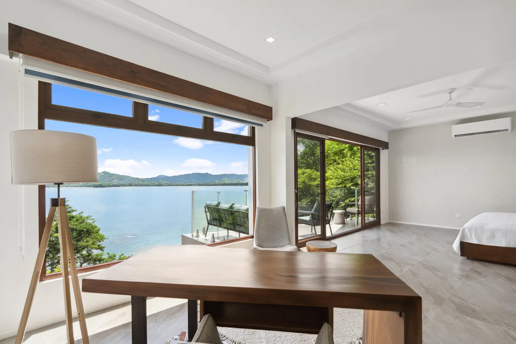 A bright bedroom and sitting area open onto a balcony overlooking the water.