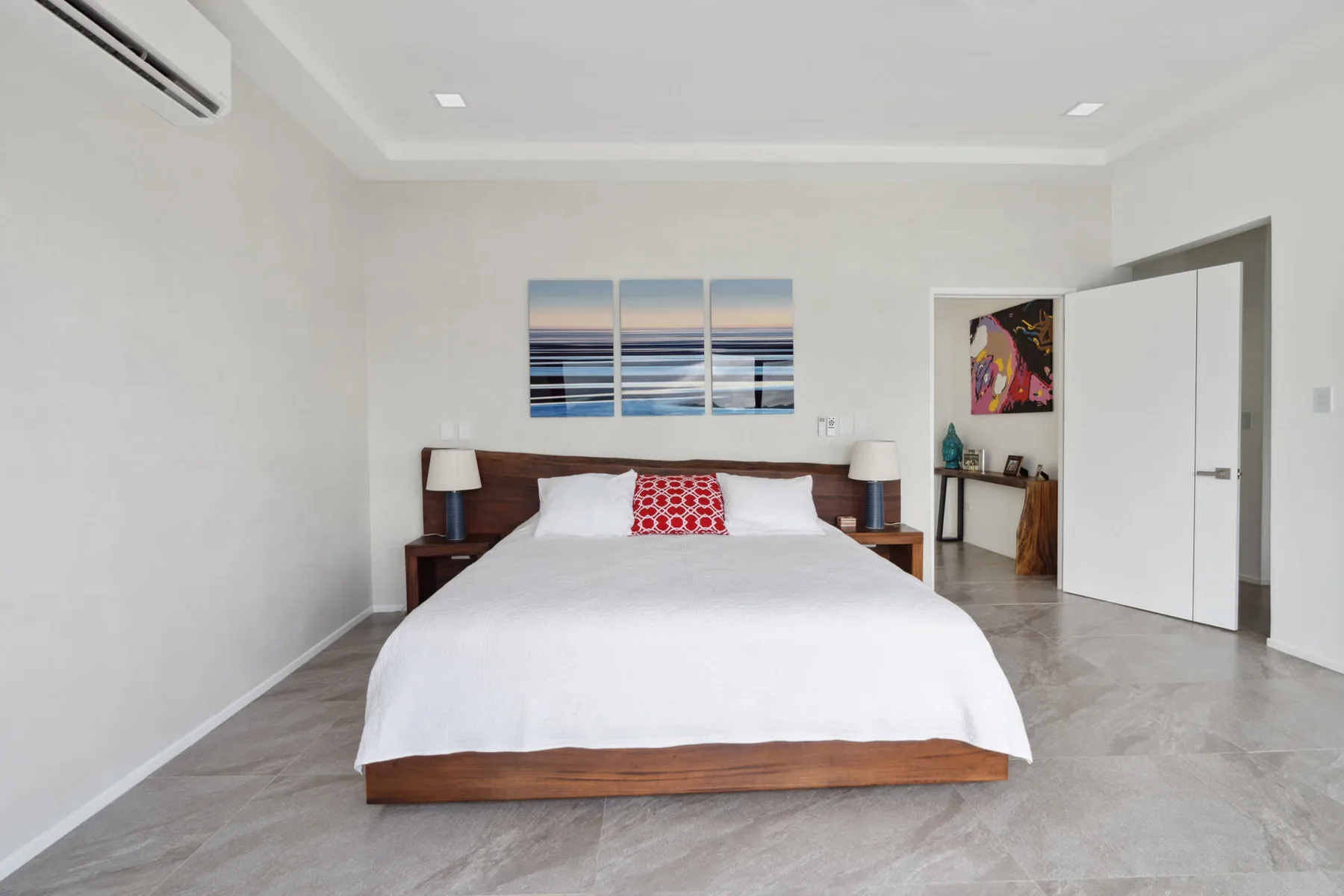 A bedroom with a bed dressed in white linens and artwork above the headboard.
