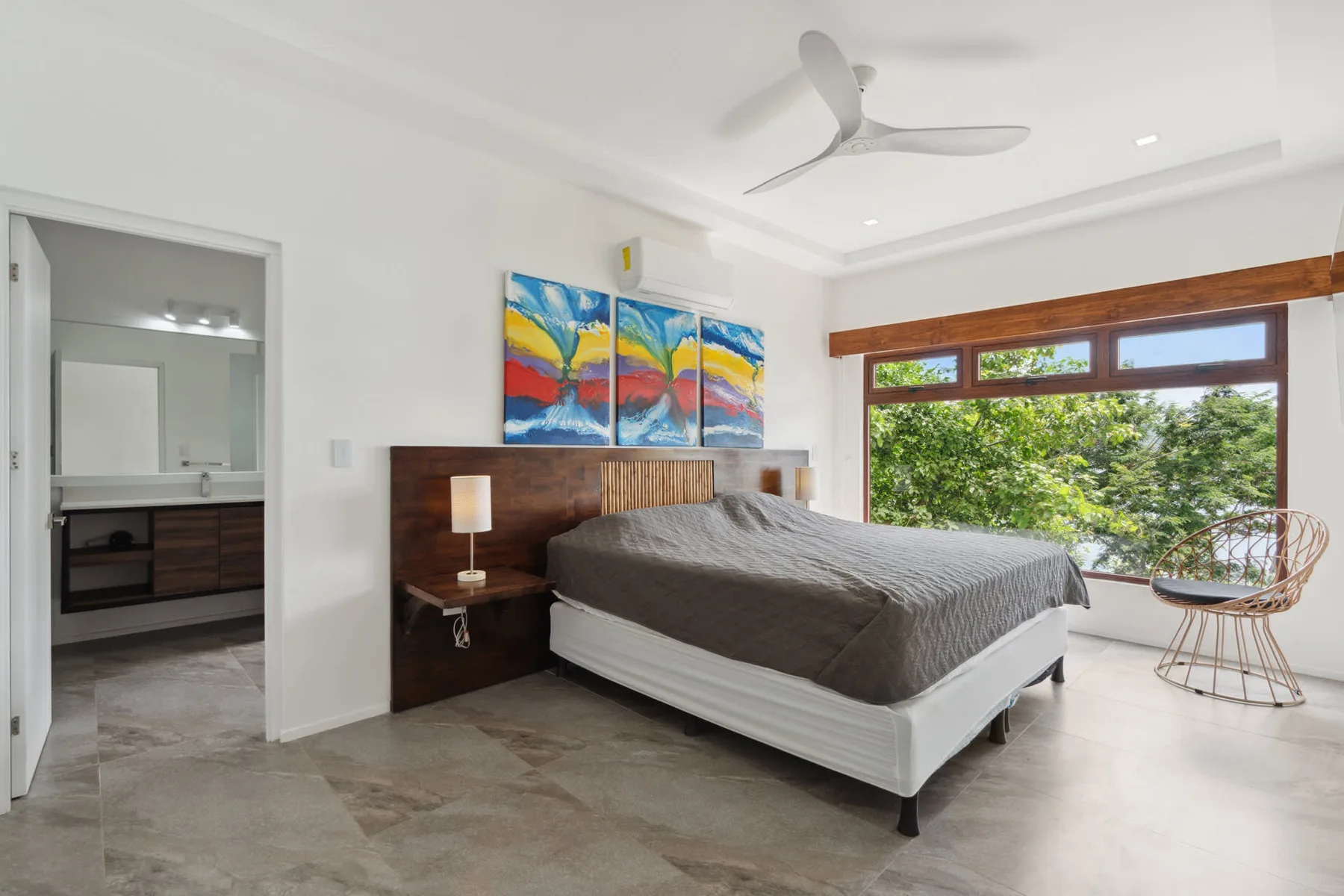 A bedroom with a bed beneath colorful artwork and a large window.