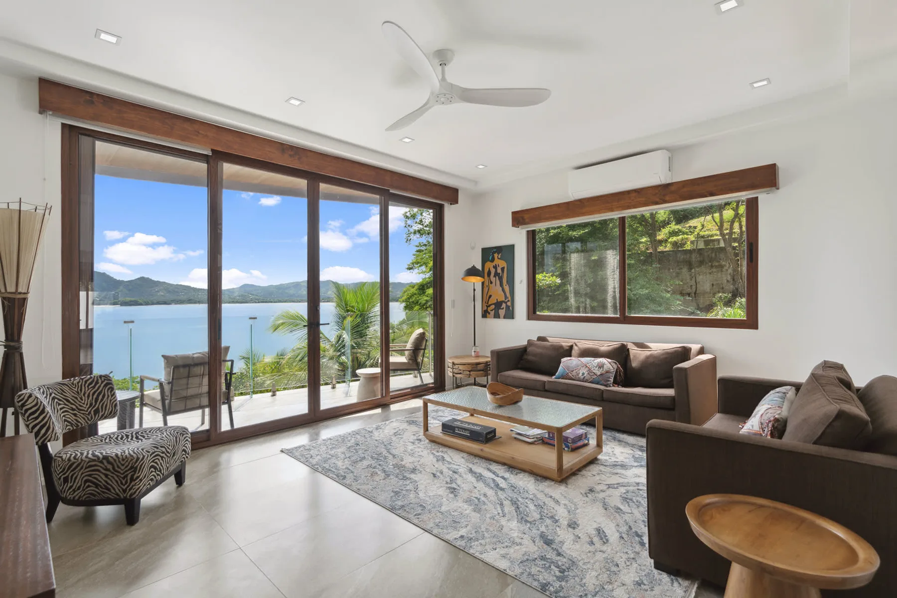 A living room with seating and a coffee table beside large windows overlooking the water.
