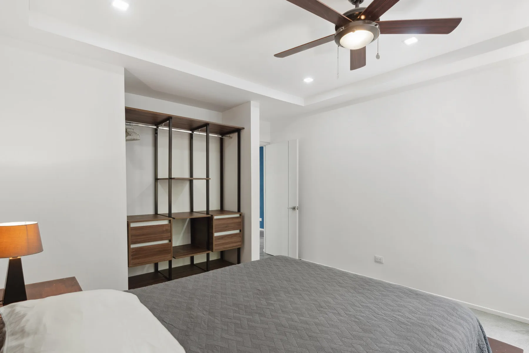 A bedroom with a bed, open shelving, and a ceiling fan.