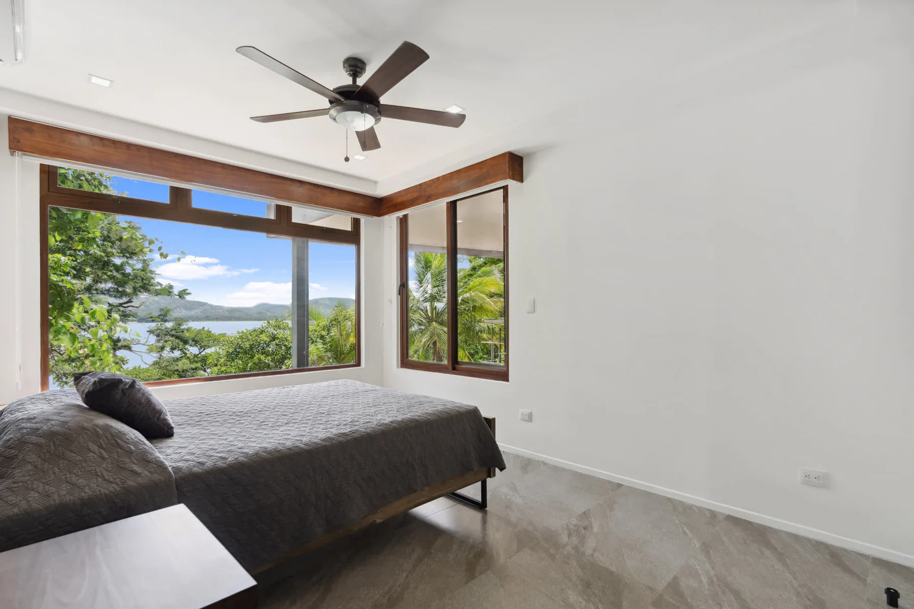 A bedroom with a bed beside large windows overlooking greenery and water.