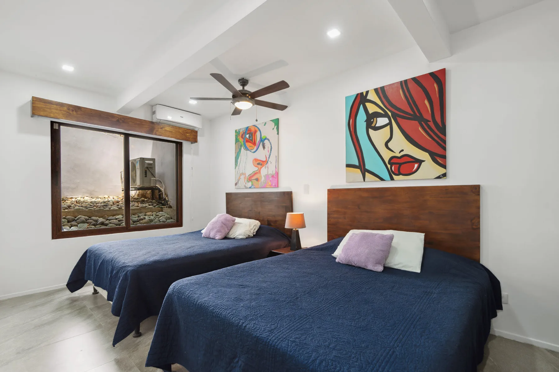 A bedroom with two beds dressed in dark blue covers and colorful wall art.