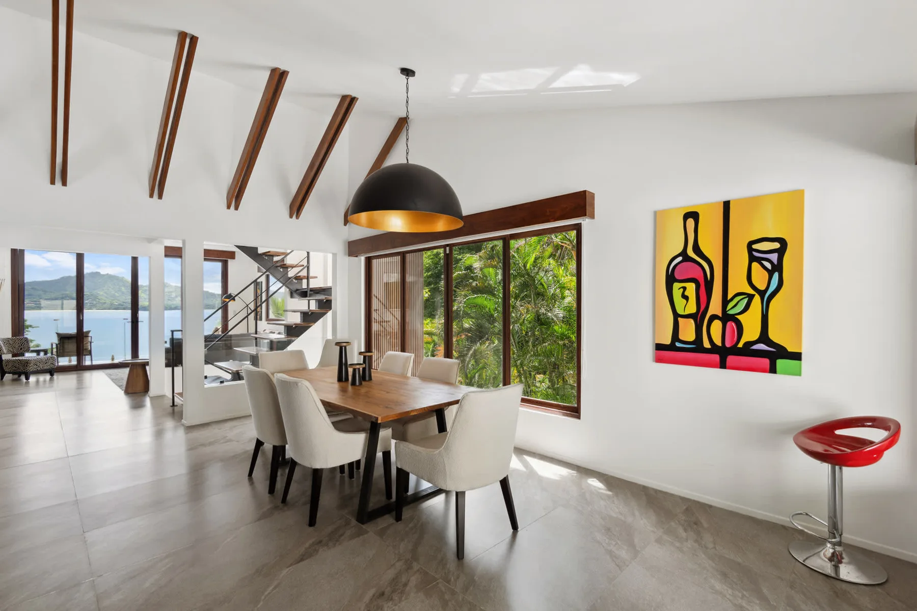 A bright dining area with a wooden table, seating, and large windows overlooking greenery.