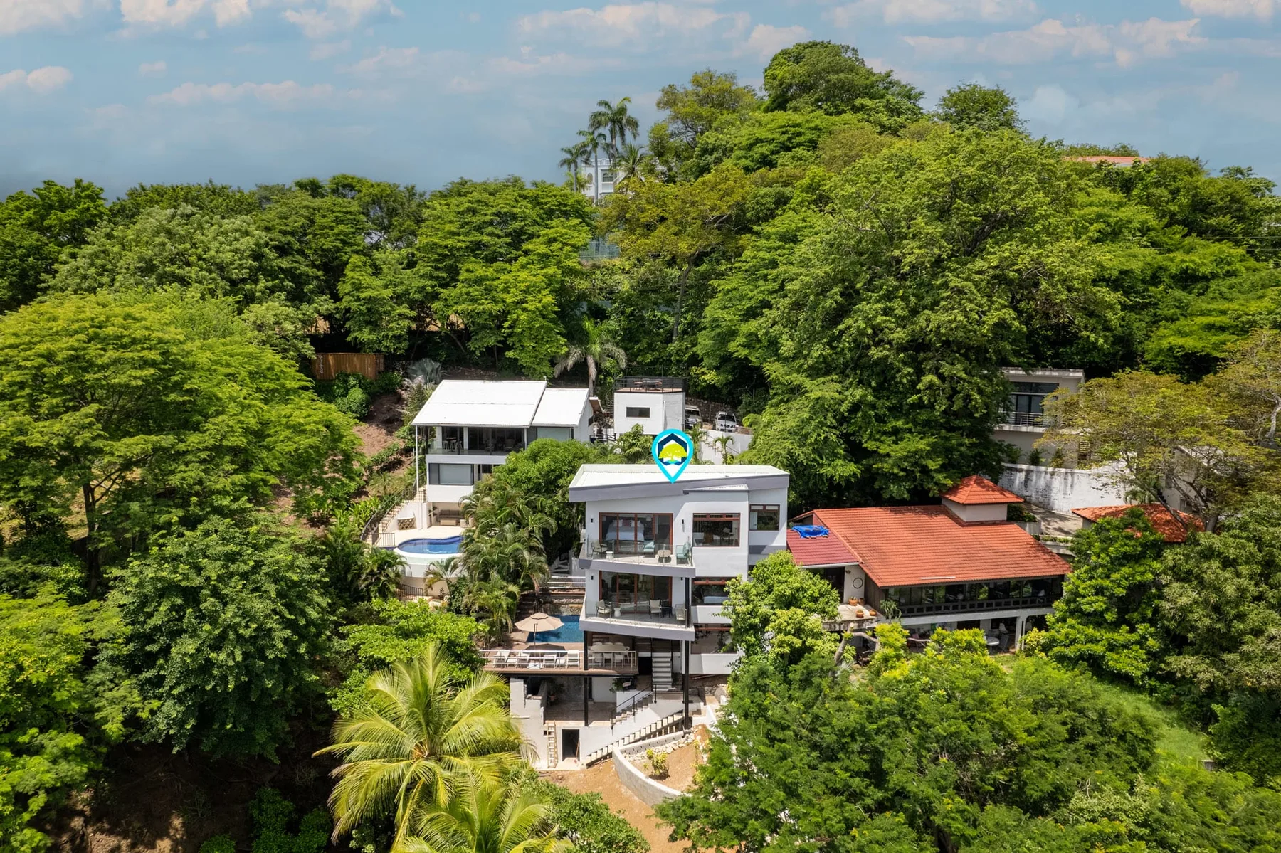 An aerial view of a modern house surrounded by dense green trees.