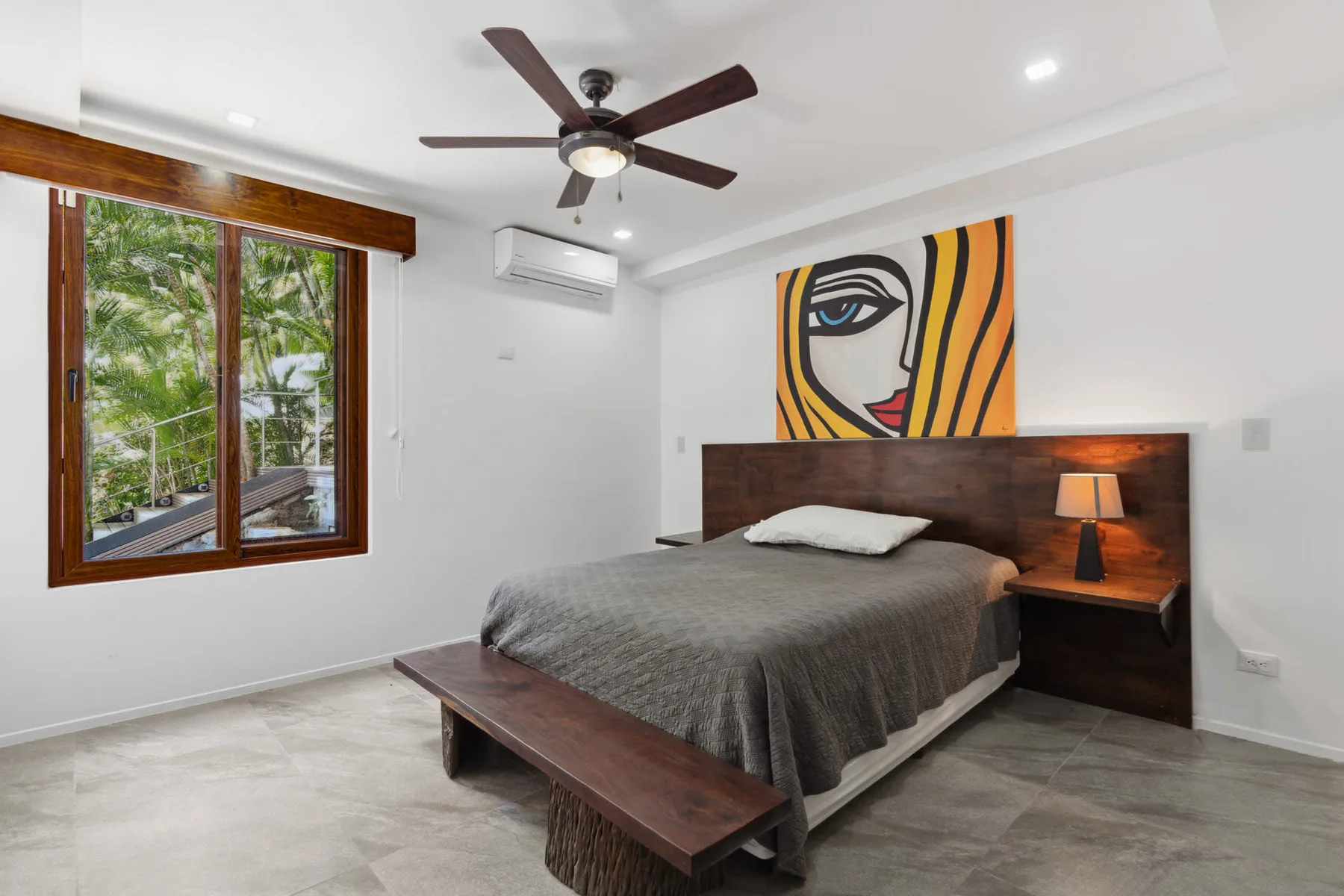 A bedroom with a bed, wooden headboard, and colorful artwork above it.