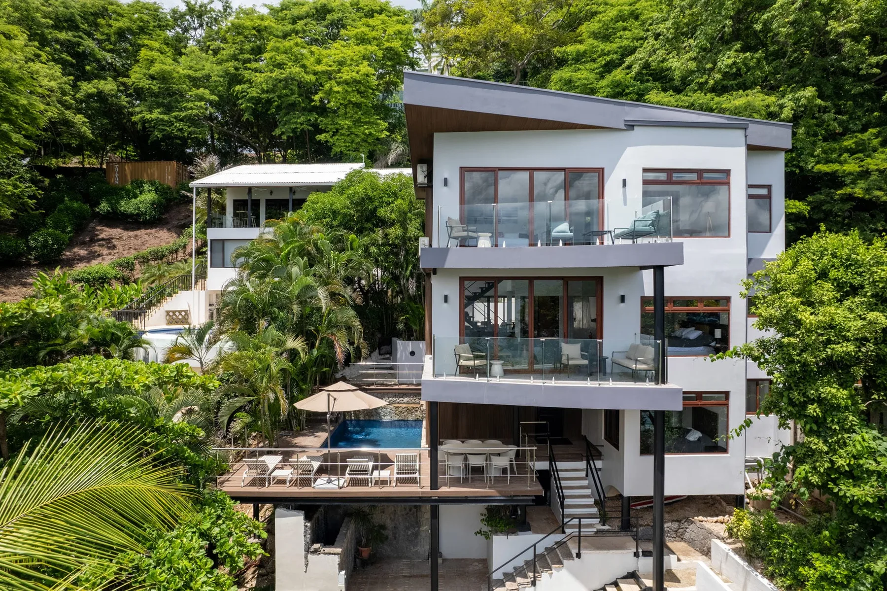 A modern multi-level house sits among dense green trees.