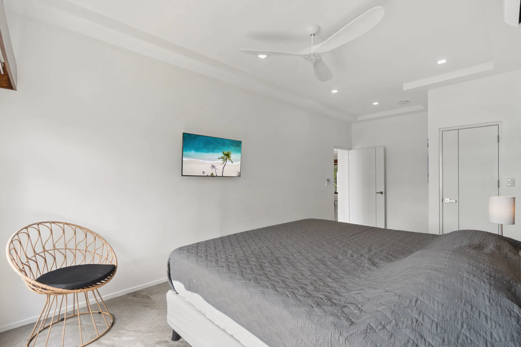 A bright bedroom with a large bed and a television mounted on the wall.