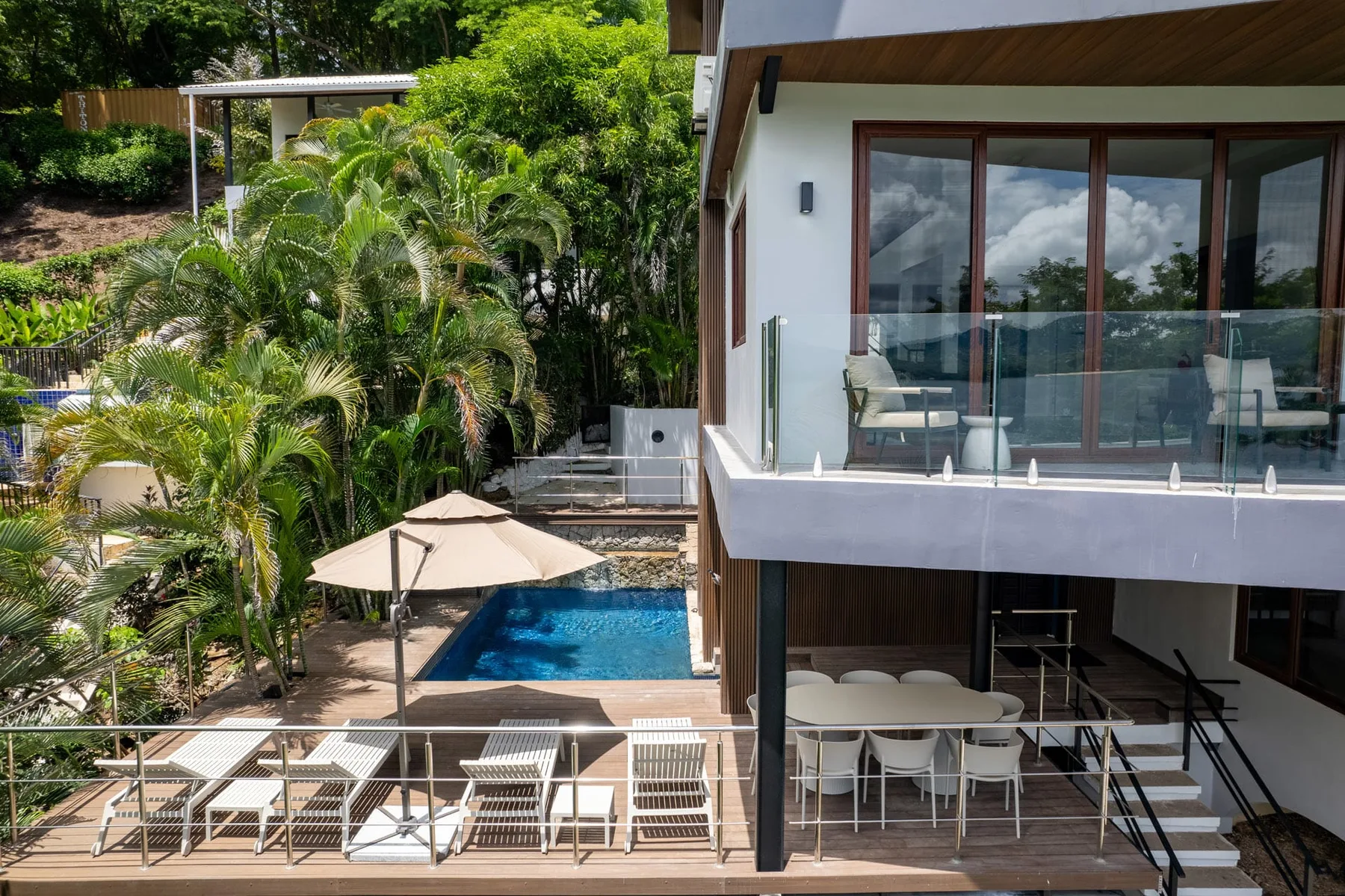 A modern house overlooks a swimming pool and outdoor dining area amid lush greenery.
