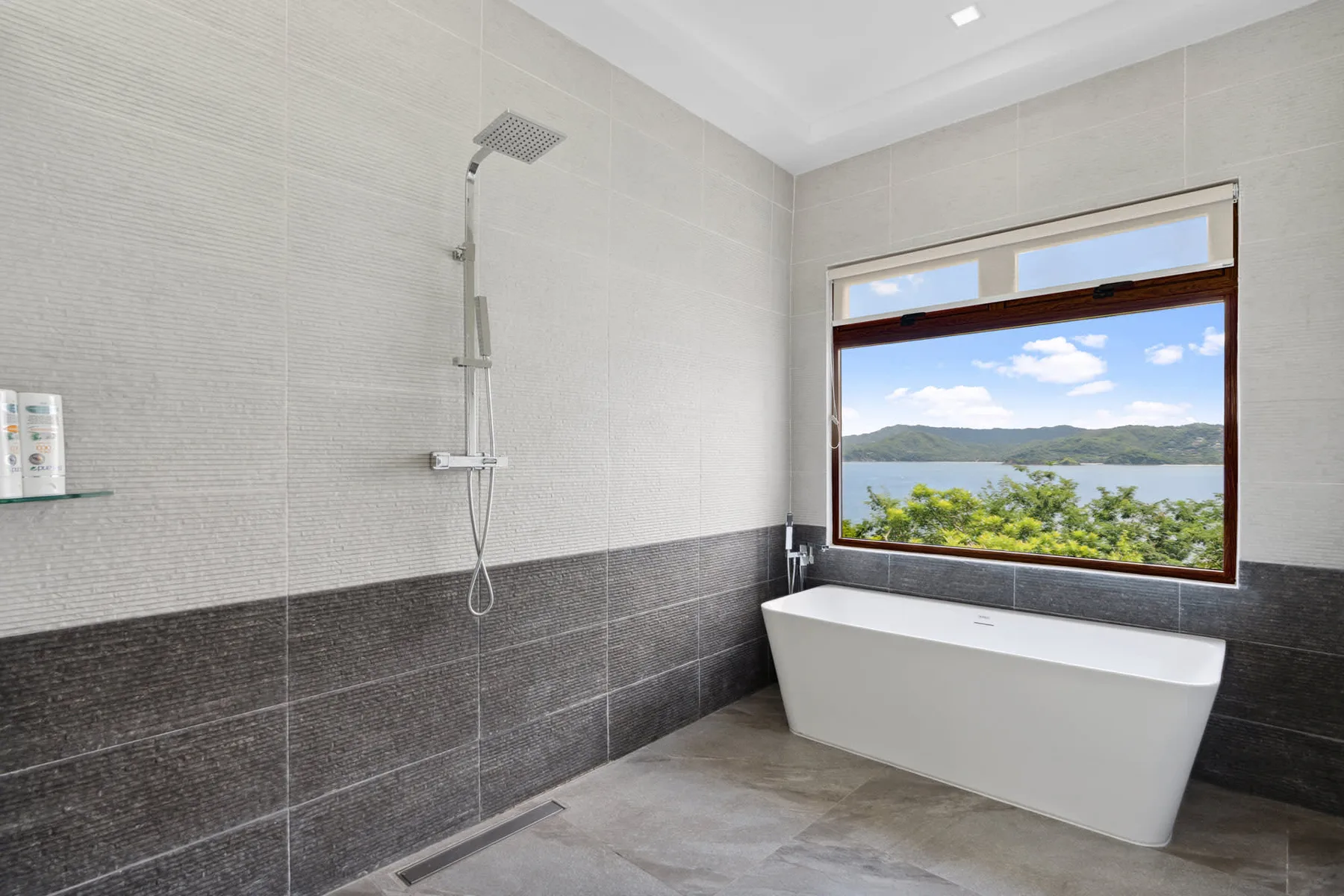 A bright bathroom with a bathtub and a large window overlooking a green landscape.