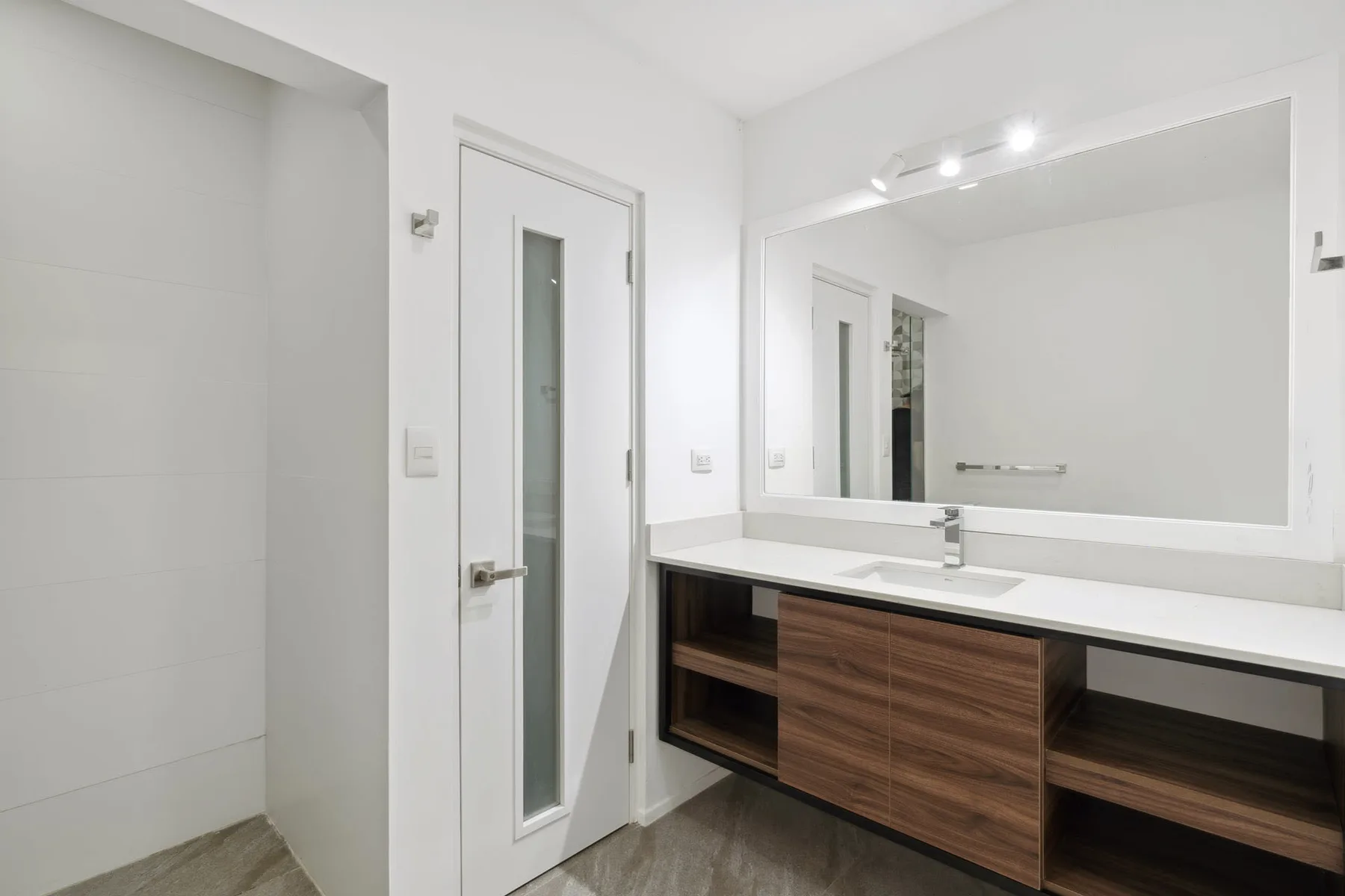 A bright bathroom vanity with a wide mirror and white countertop.