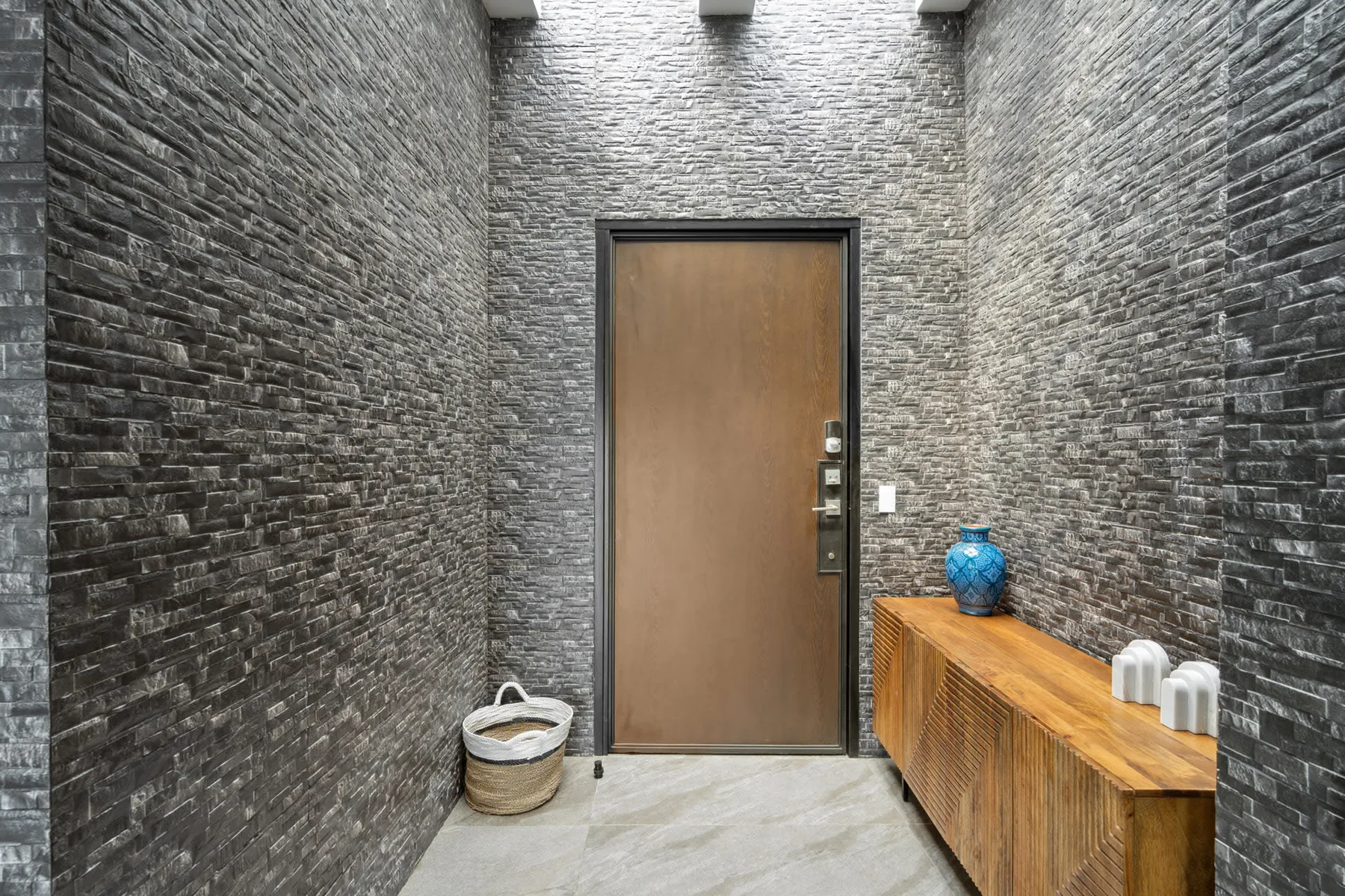 A stone-walled entryway has a brown door and a wooden console table.
