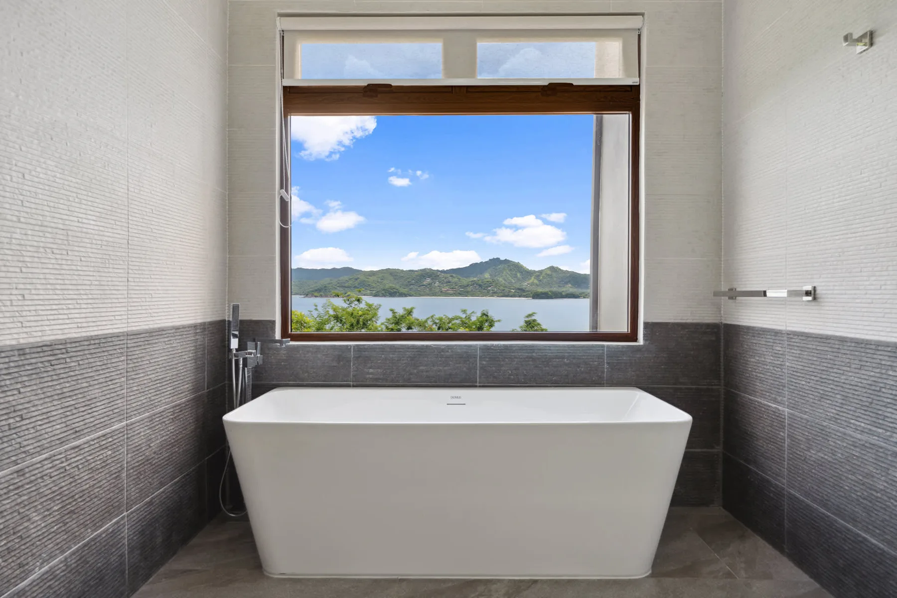 A bathroom with a freestanding bathtub beneath a large window overlooking a lake.